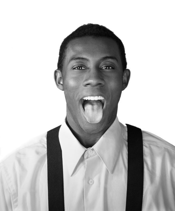 A man with braces and suspenders sticking out his tongue.